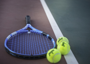 Three tennis balls beside a tennis racket on the floor
